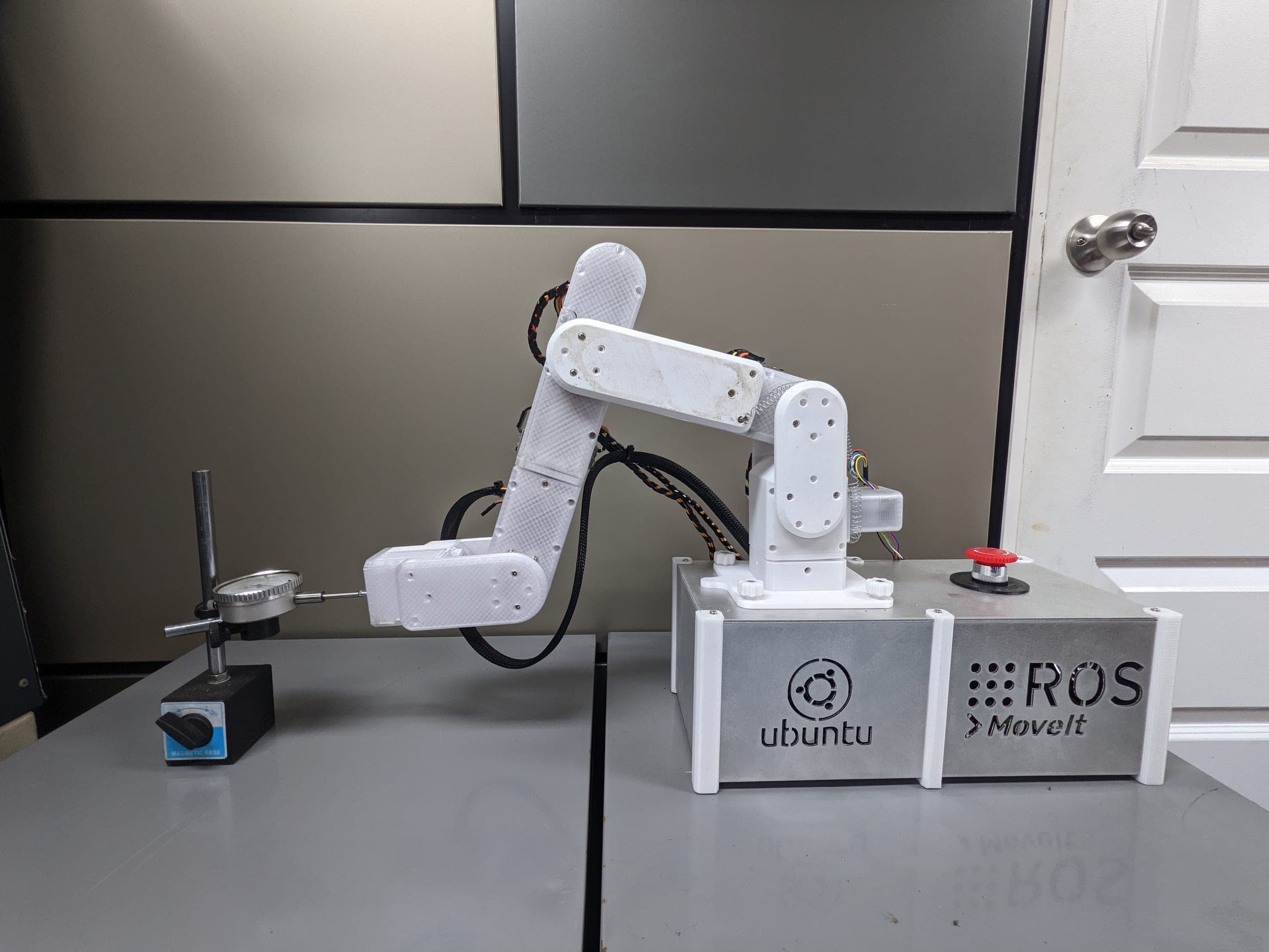 The robotic arm in a retracted test pose beside the dial indicator measurement frame